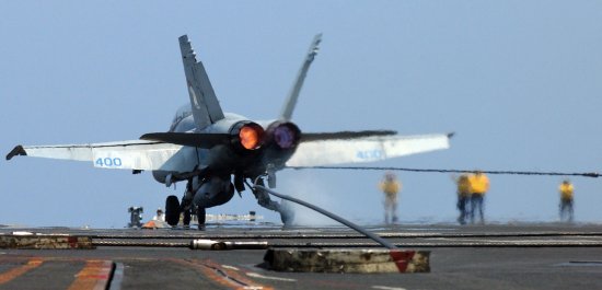 F-18 with afterburners lit as it catches an arresting cable
